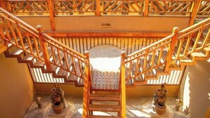 A wooden staircase with a handrail, leading to a landing with a bench. There are two decorative vases at the base of the stairs. - Spring Breeze Inn (Shangri-La)