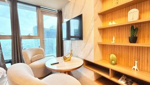 Ein modernes Hotelzimmer mit großem Fenster, einem Flachbildfernseher, einem runden Couchtisch und einem Holzbücherregal mit Dekoration.