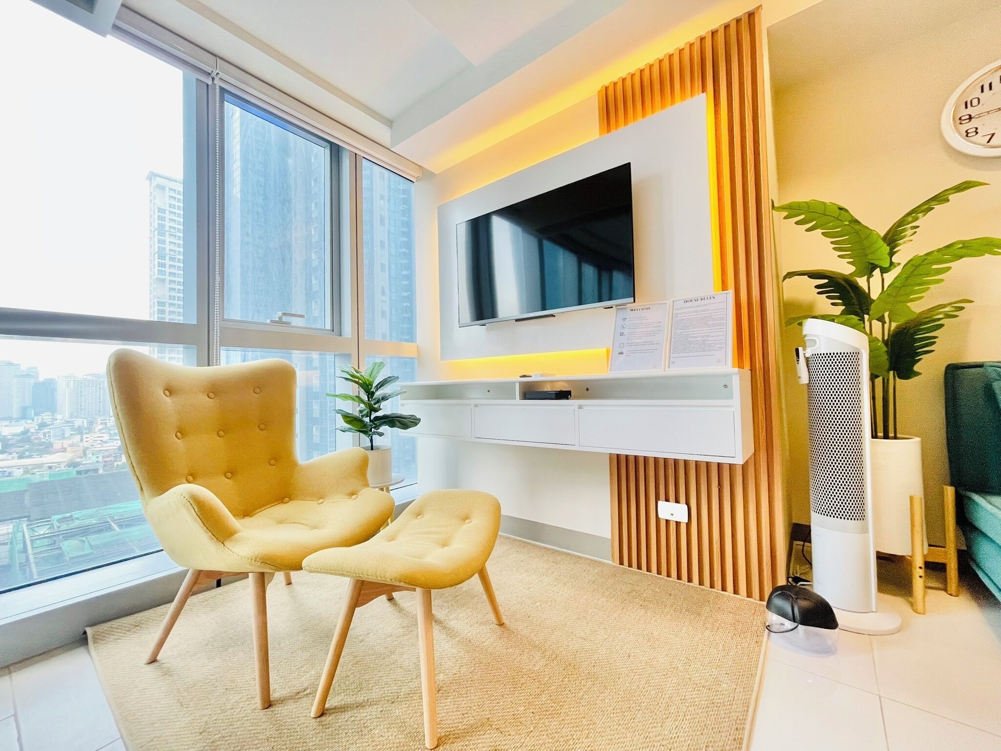A modern living room with a large window, a flat-screen TV, a yellow armchair, a small table, and a potted plant.