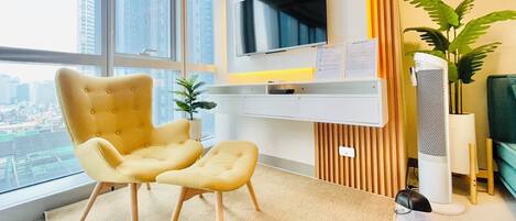 Un salón moderno con un ventanal grande, un televisor de pantalla plana, un sillón amarillo, una mesita y una planta en maceta.