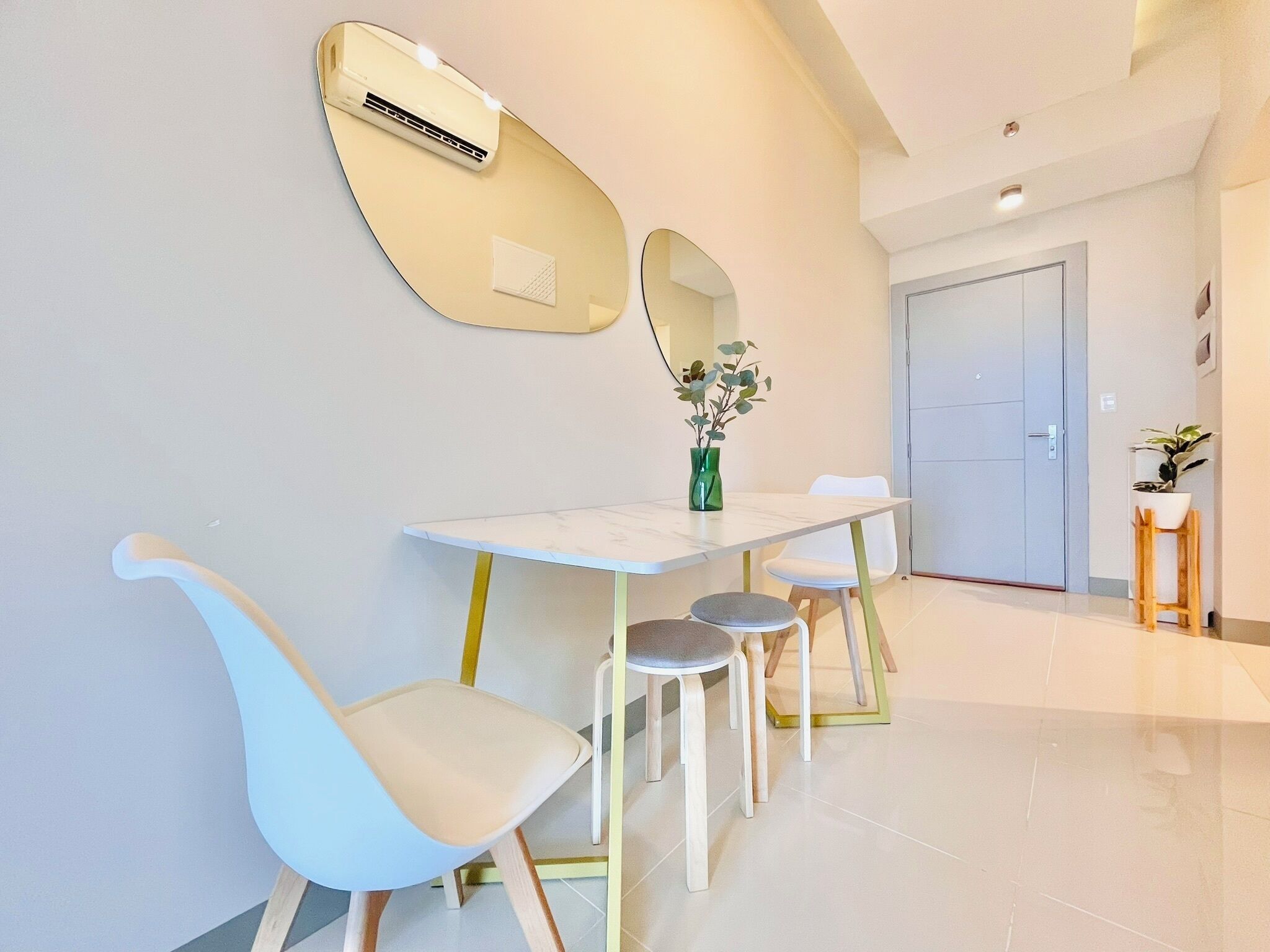 A modern hotel room with a marble-topped table, two chairs, a mirror, and a potted plant.