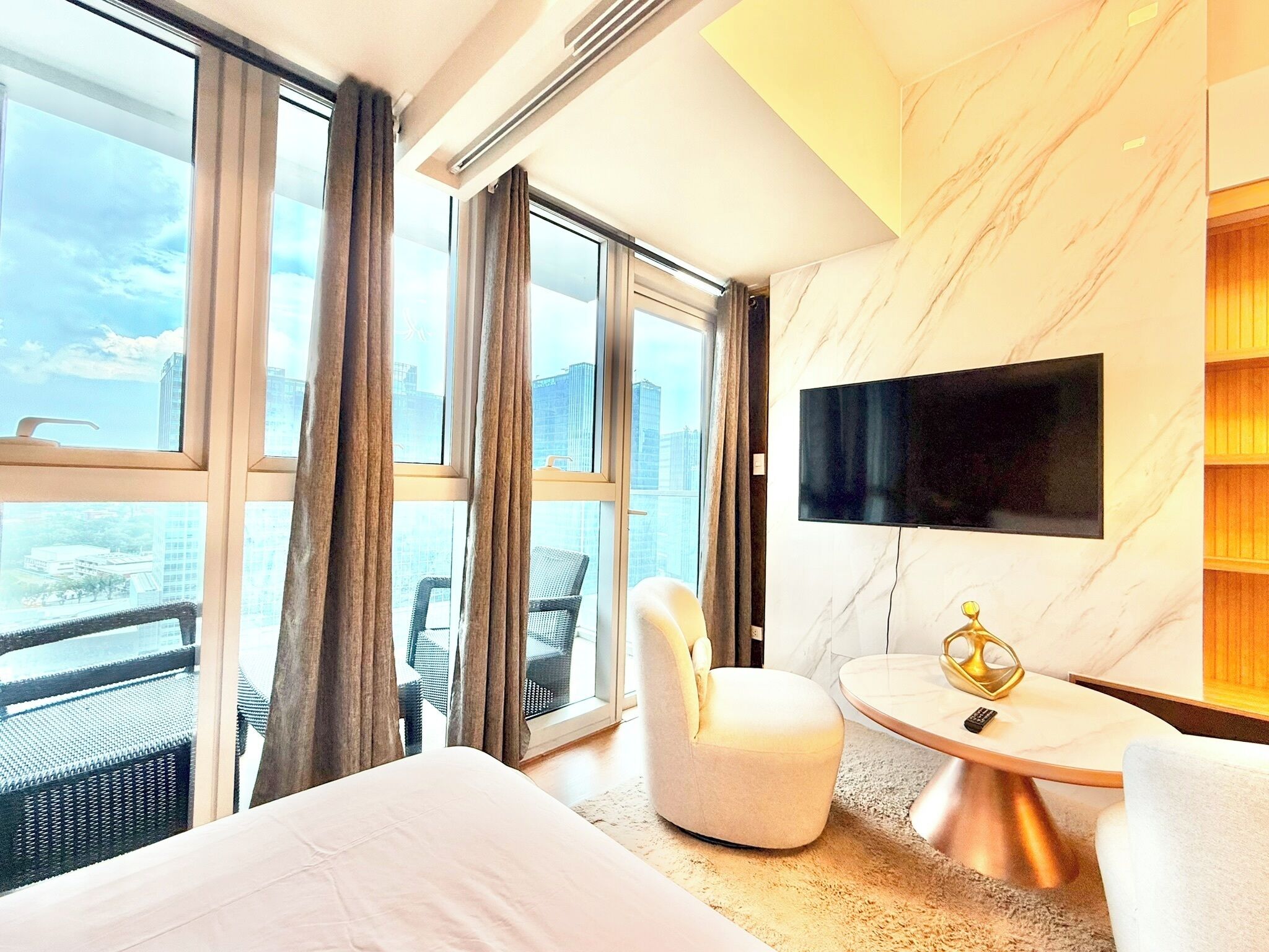 Ein Hotelzimmer mit großem Fenster, einem Flachbildfernseher, einem runden Tisch, einem Sessel und einem Bett.