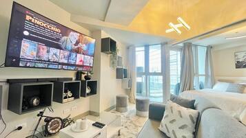 A modern hotel room with a large flat-screen TV, a sofa, a bed, and a window with a city view.
