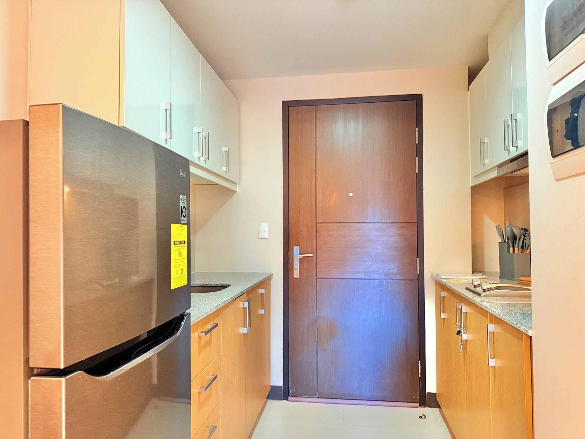 A compact kitchen with a stainless steel refrigerator, wooden cabinets, and a wooden door.