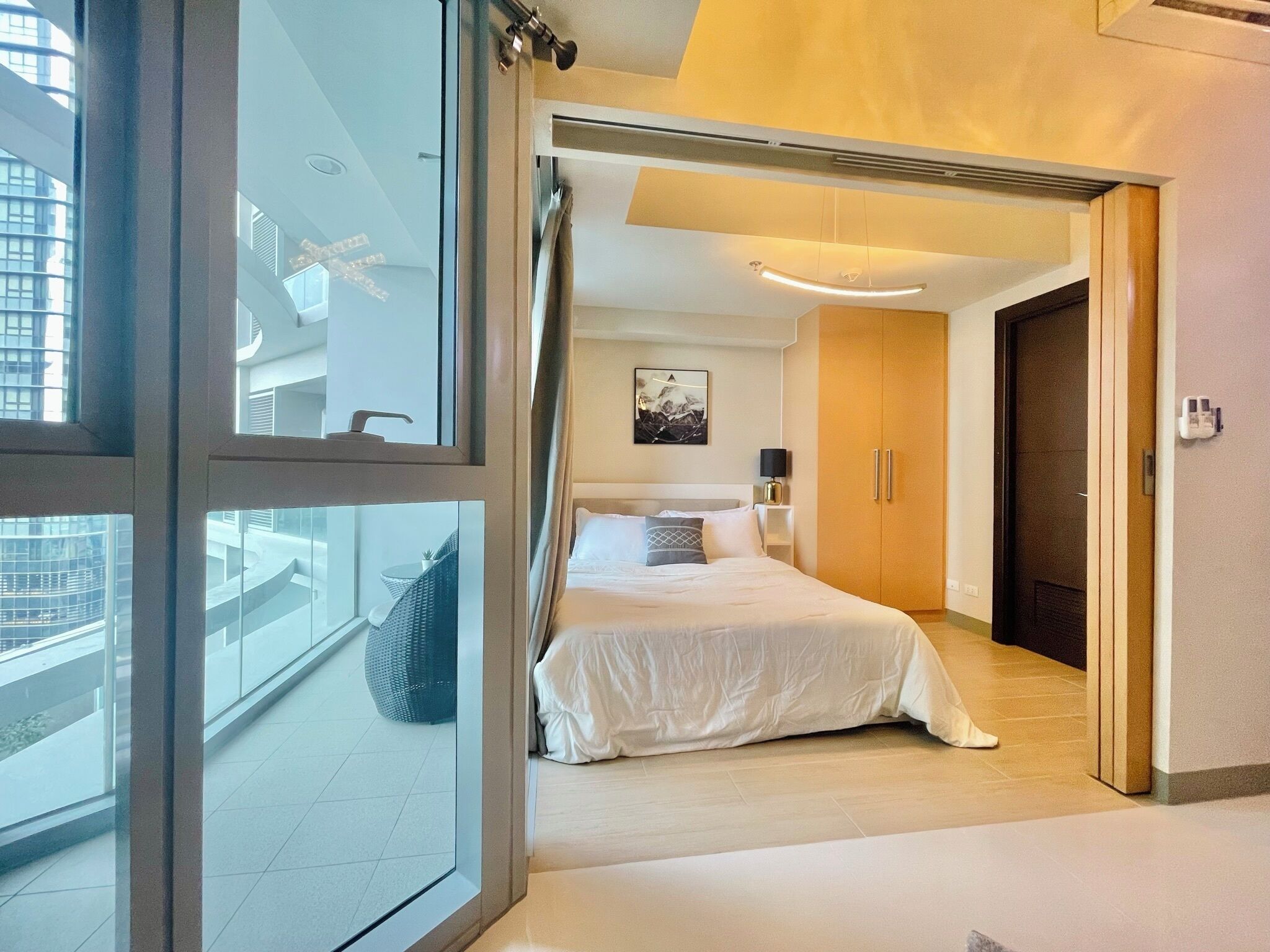 Een moderne hotelkamer met een groot bed, een nachtkastje, een wandlamp en uitzicht op de stad door een groot raam.