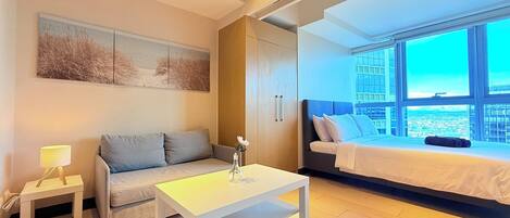 Une chambre d’hôtel moderne équipée d’un lit, d’un canapé, d’une petite table et d’une grande fenêtre donnant sur la ville.