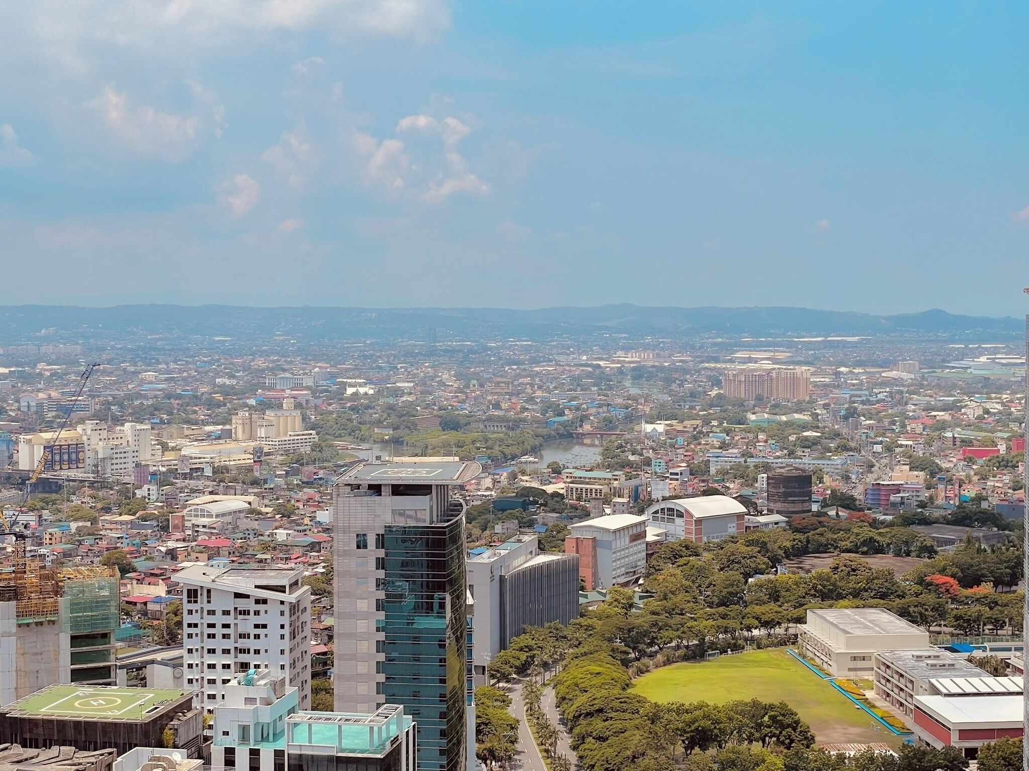 A cityscape with a mix of modern and older buildings, a large open field, and a river in the distance.