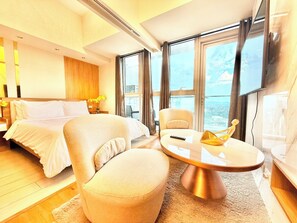 Habitación de hotel moderna con cama, sofá, una mesita redonda y ventanas amplias con vistas a la ciudad.