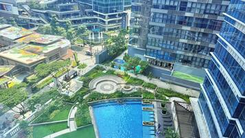 Un edificio de gran altura con piscina en la azotea, rodeado de vegetación y una fuente.
