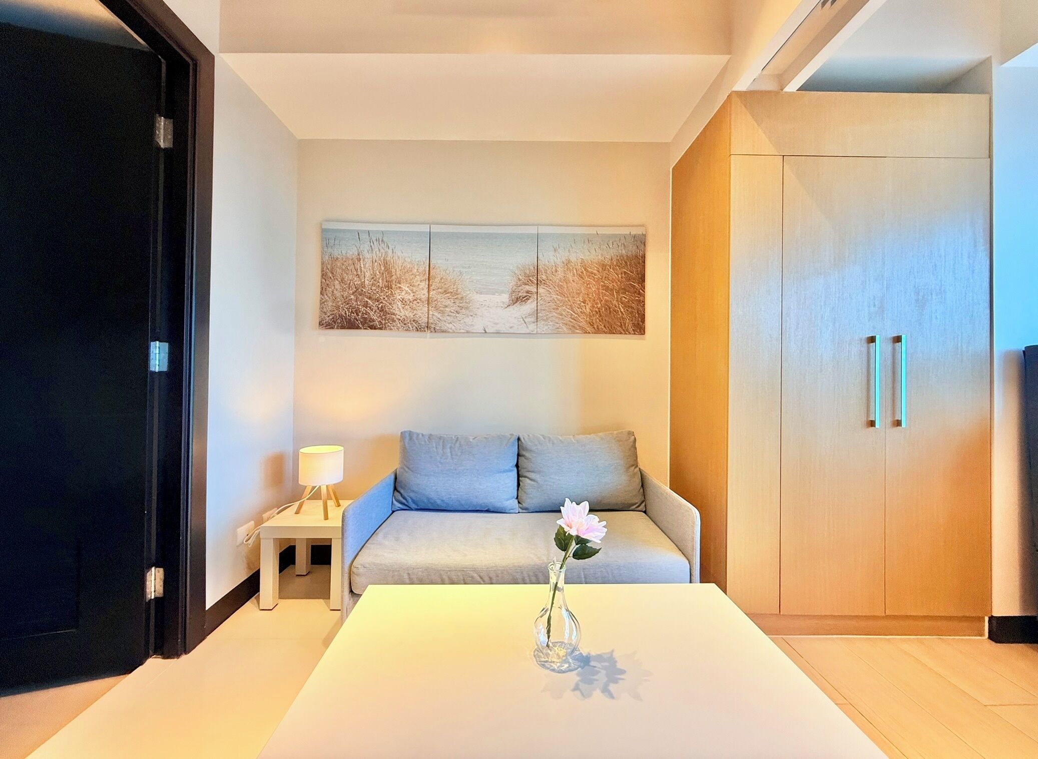 A modern room with a sofa, a table with a vase, a lamp, and a painting on the wall.