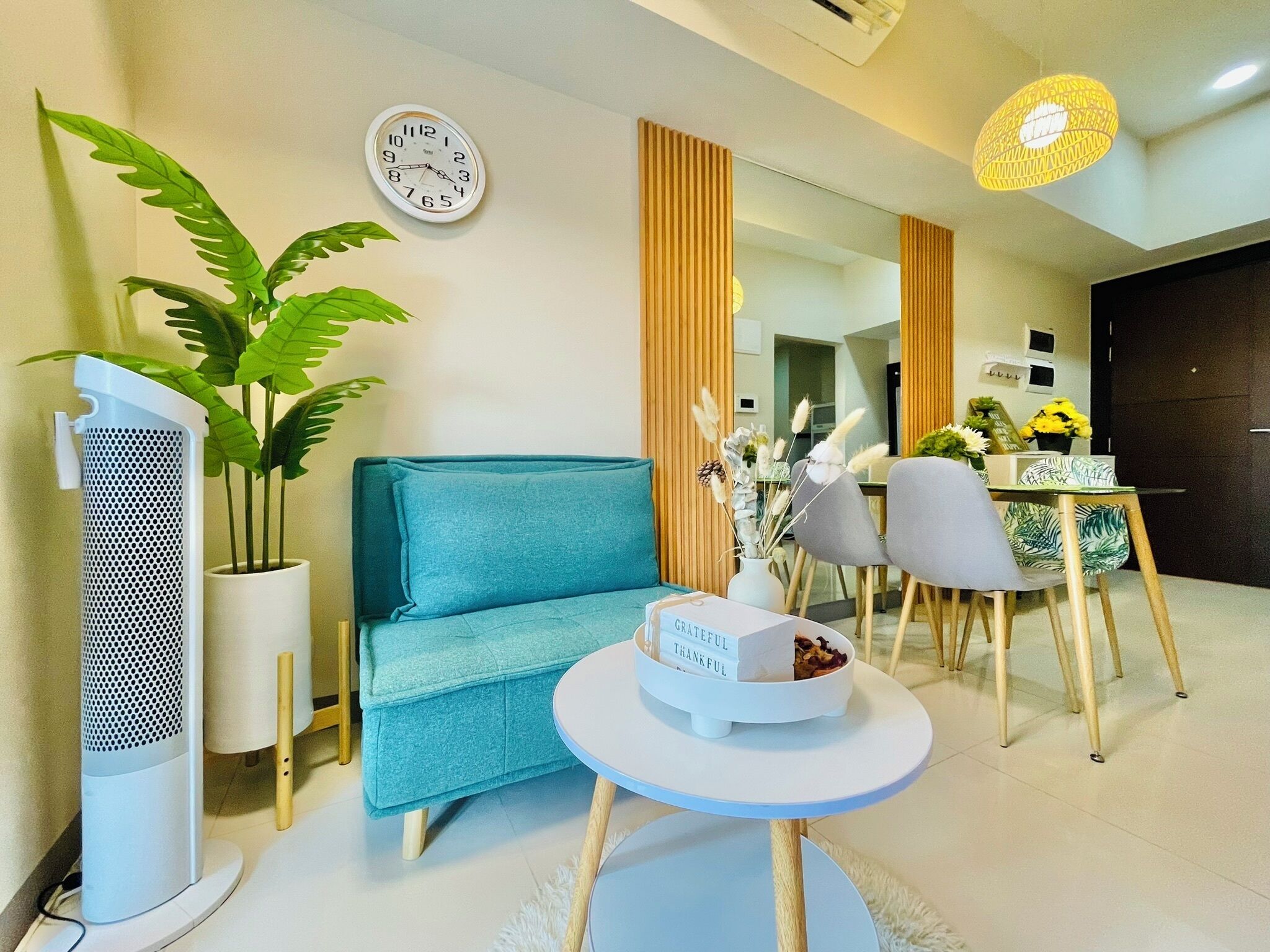 Un salon moderne comprenant un canapé, une table basse, un téléviseur, une plante en pot, une horloge et un coin repas avec des chaises et une table.