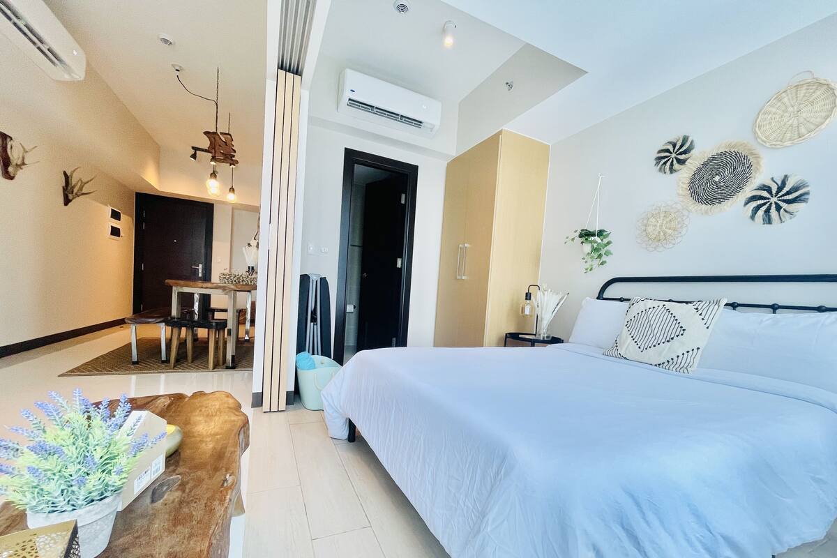 A modern hotel room with a large bed, a dining area with a table and chairs, and a separate entrance.