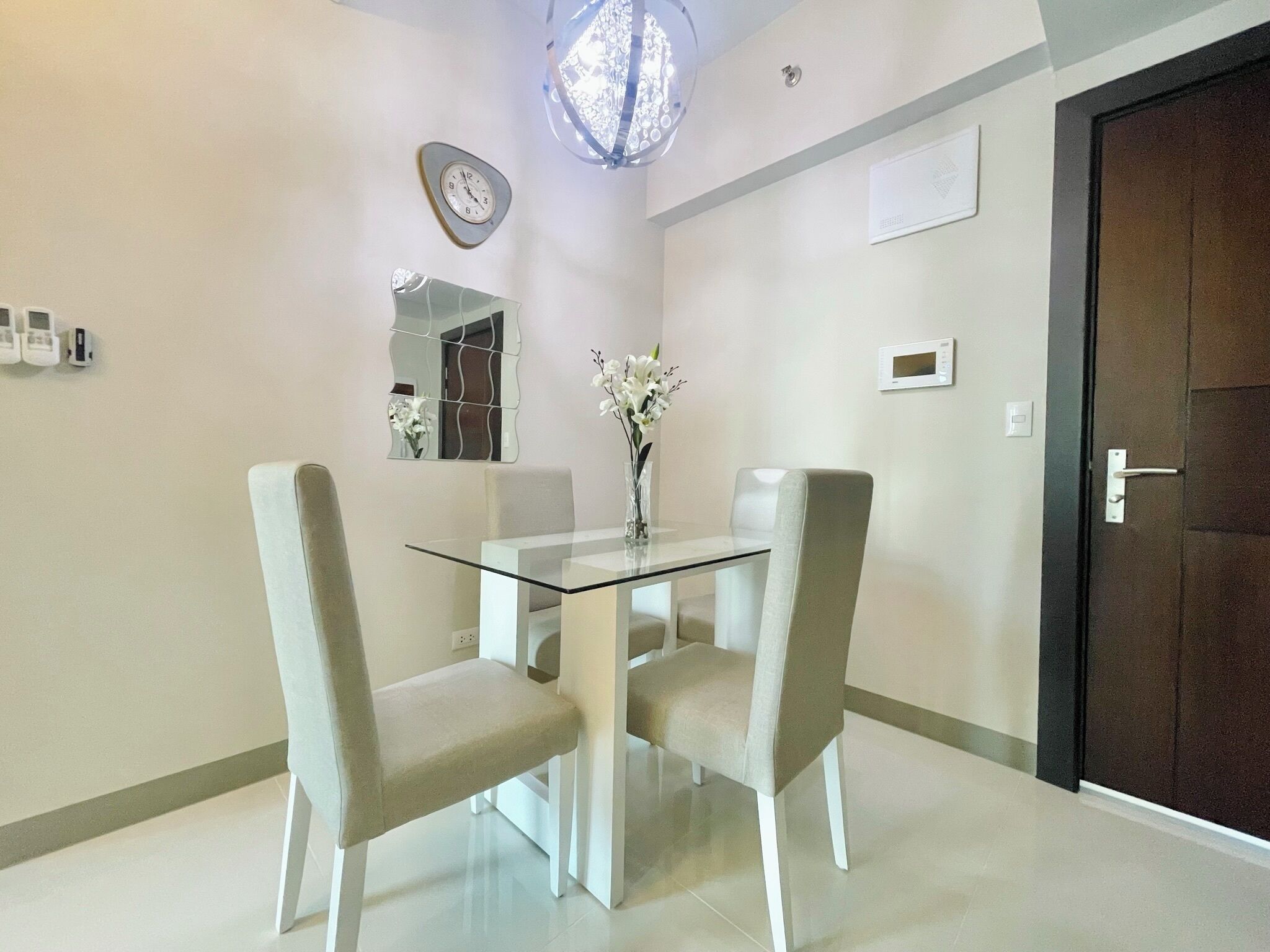 Un coin repas avec une table en verre et quatre chaises, un miroir décoratif, un vase avec des fleurs et une porte avec une poignée.