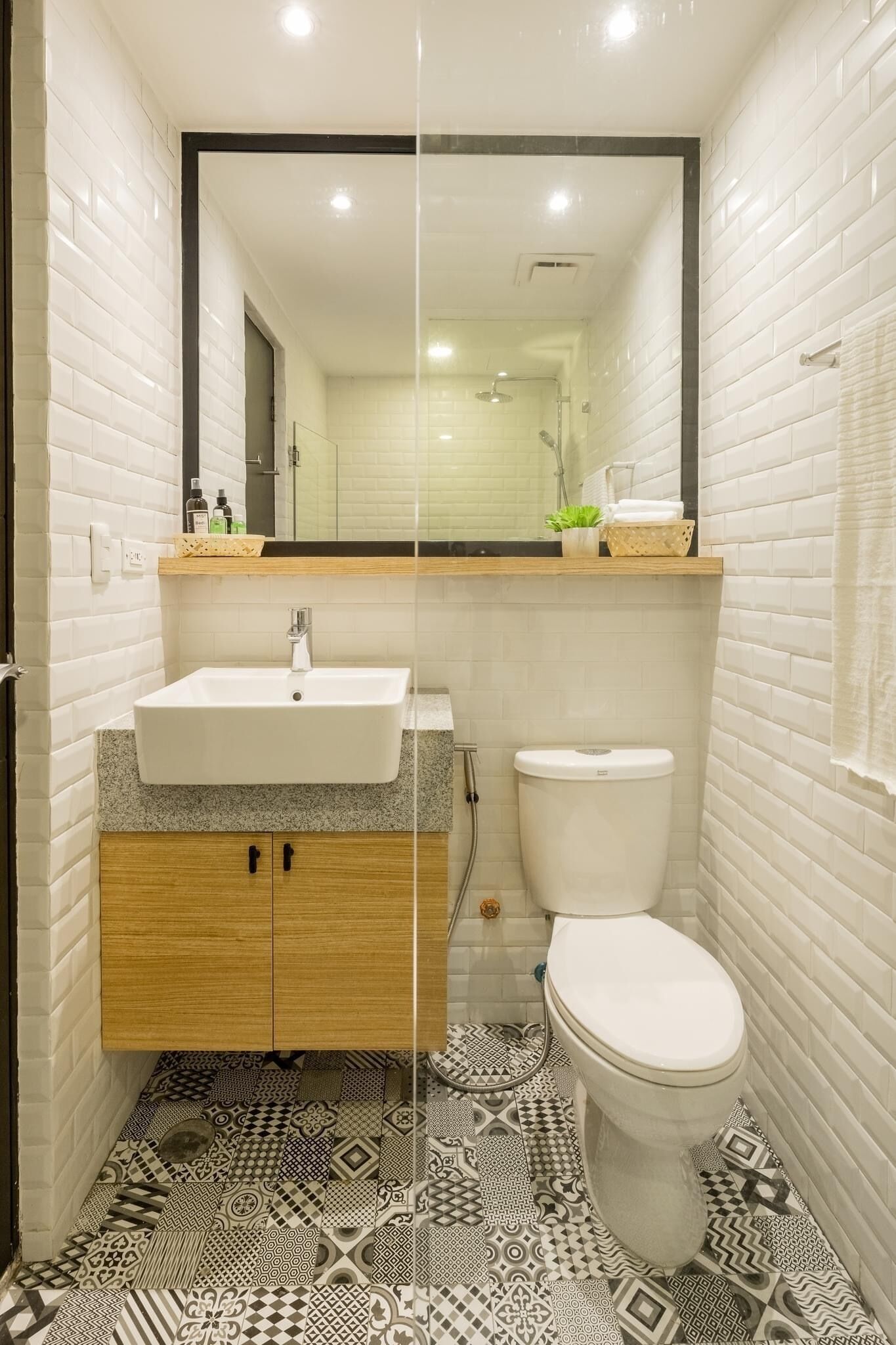 A bathroom with white subway tiles, a white sink, a toilet, and patterned floor tiles.