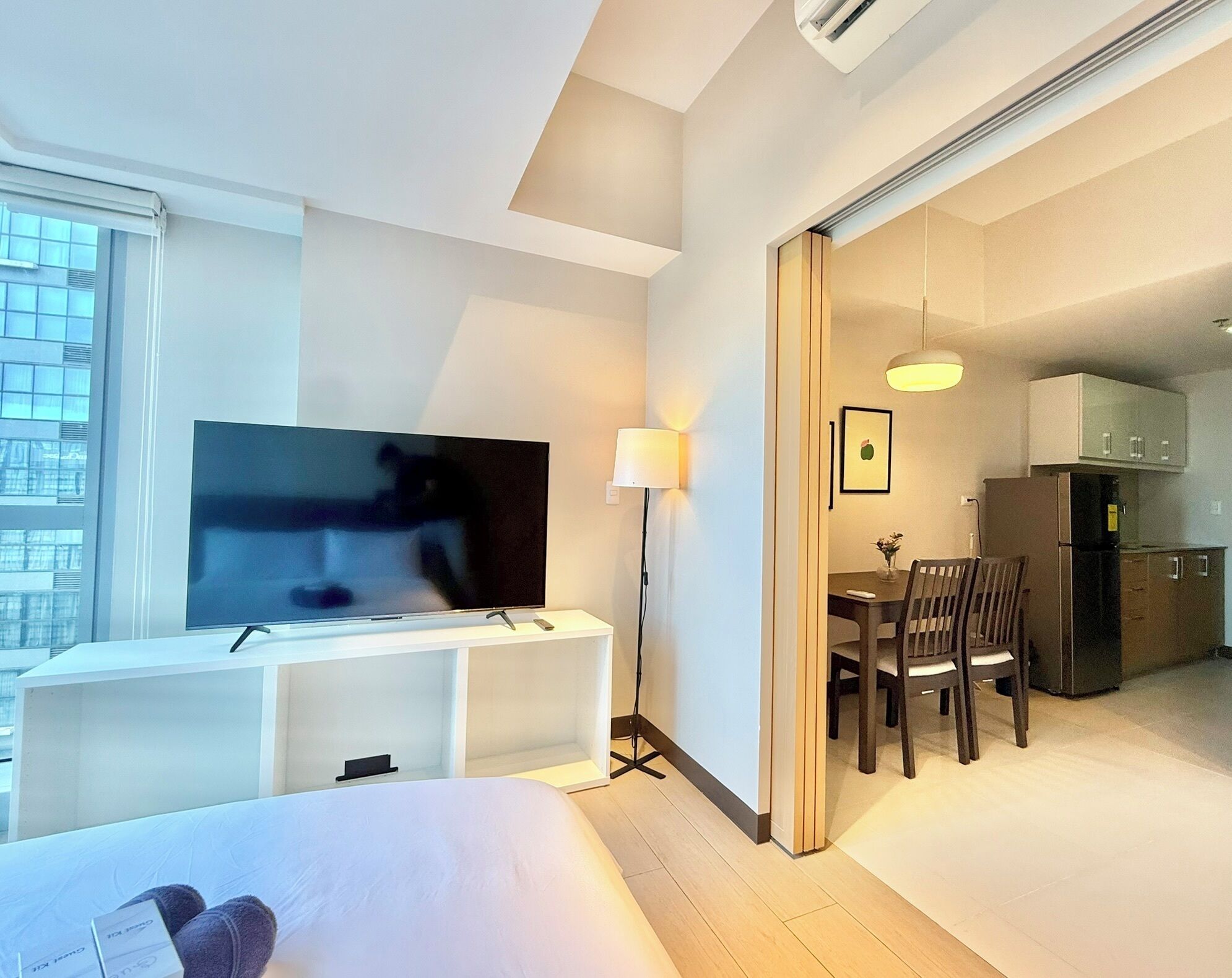 Habitación de hotel con cama, televisor, escritorio, silla, lámpara y una zona de cocina.