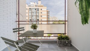 A balcony with a table, chairs, a potted plant, and a view of buildings.