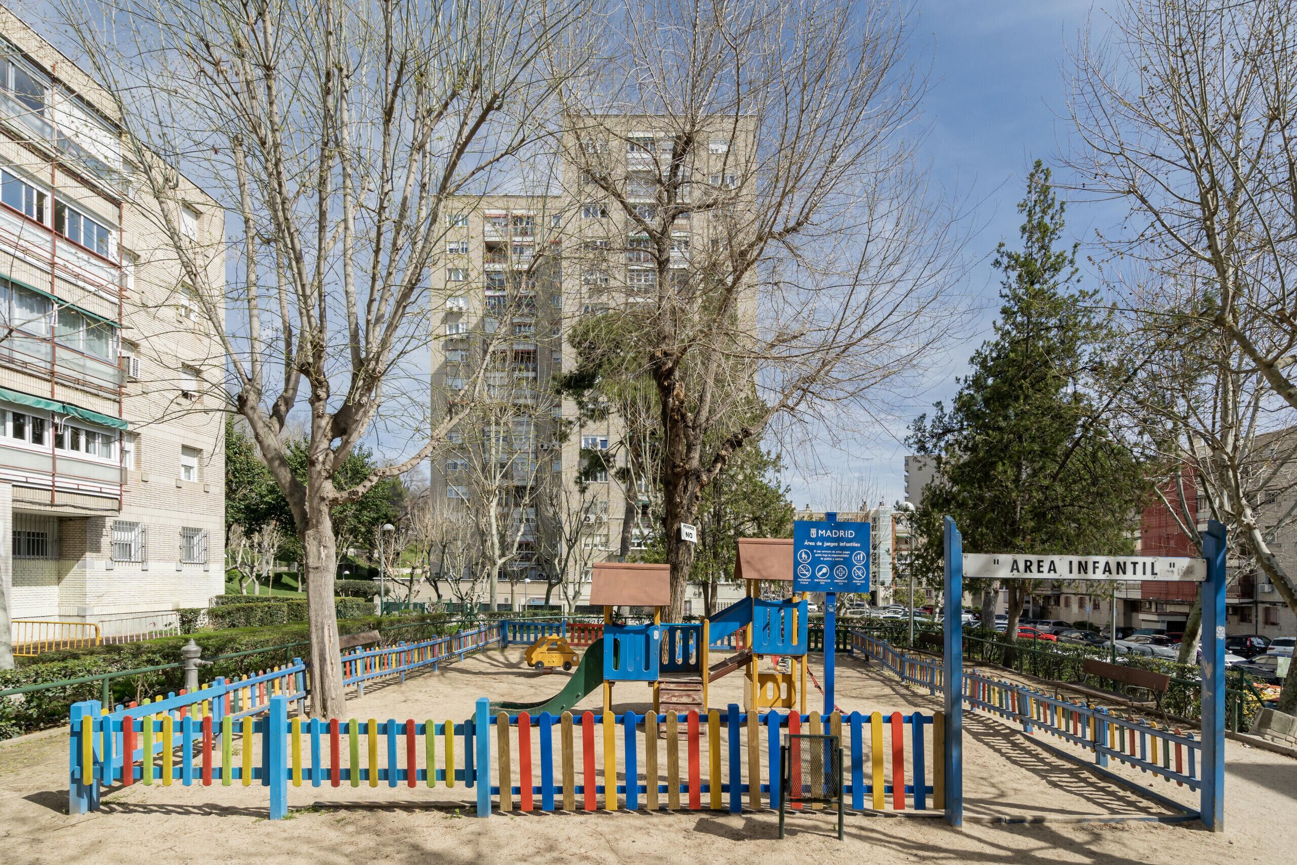 A playground with a blue fence, a slide, and a climbing structure.