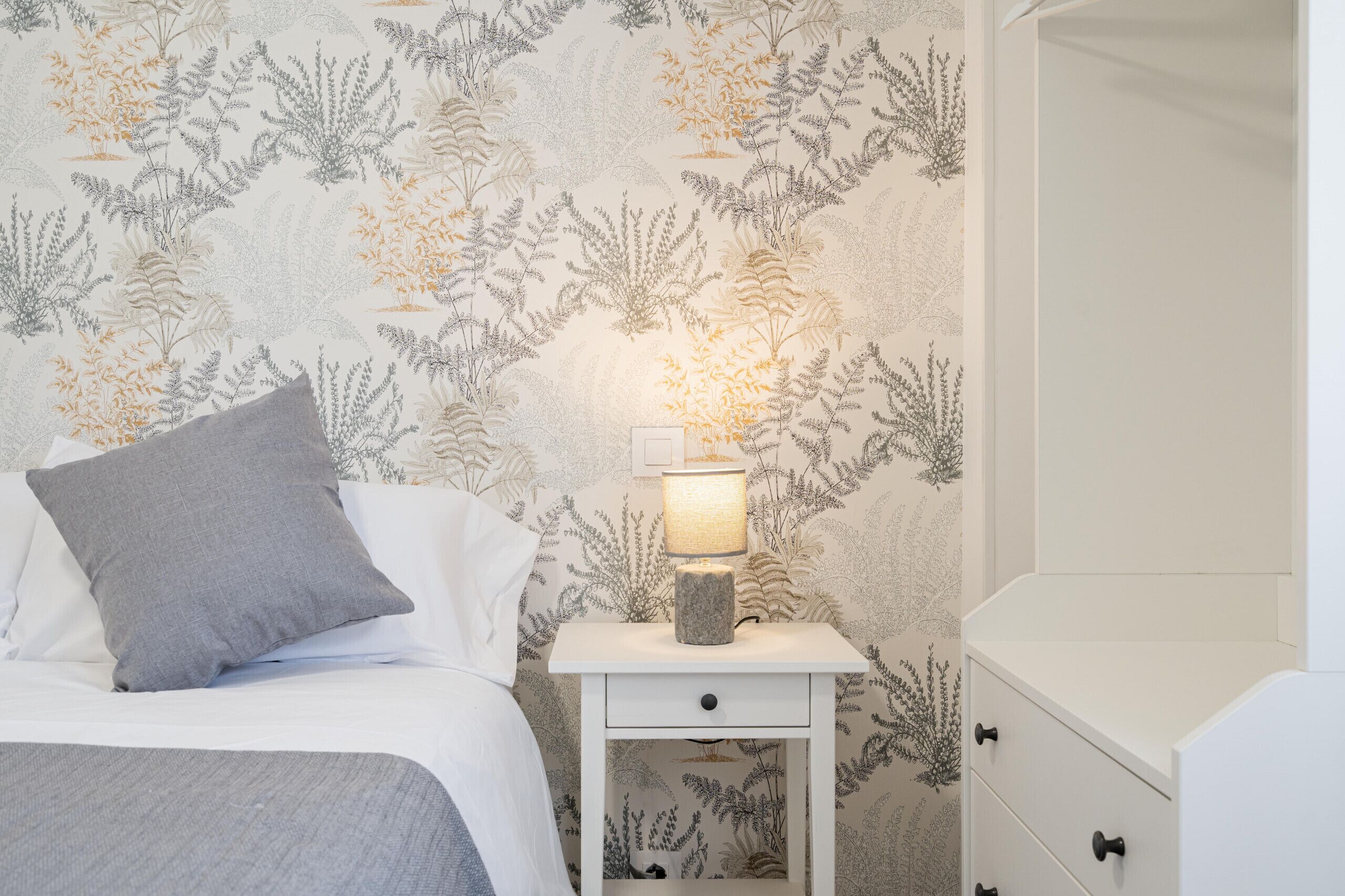 Un letto rifatto con un cuscino grigio e un comodino bianco con una lampada.