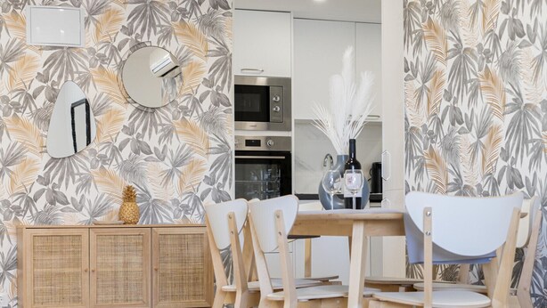 A modern living room with a dining area, featuring a wooden cabinet, a glass table, and a patterned wallpaper.