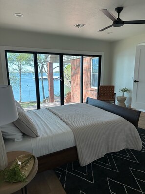Ein Schlafzimmer mit Bett, Deckenventilator, Blick auf das Wasser und einer Ziegelwand.