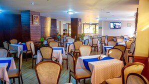 Een restaurant met meerdere tafels en stoelen, een televisiescherm aan de muur, en een bakstenen muur.