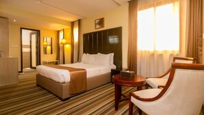 Een hotelkamer met een groot bed, een nachtkastje, een stoel en een klein tafeltje.