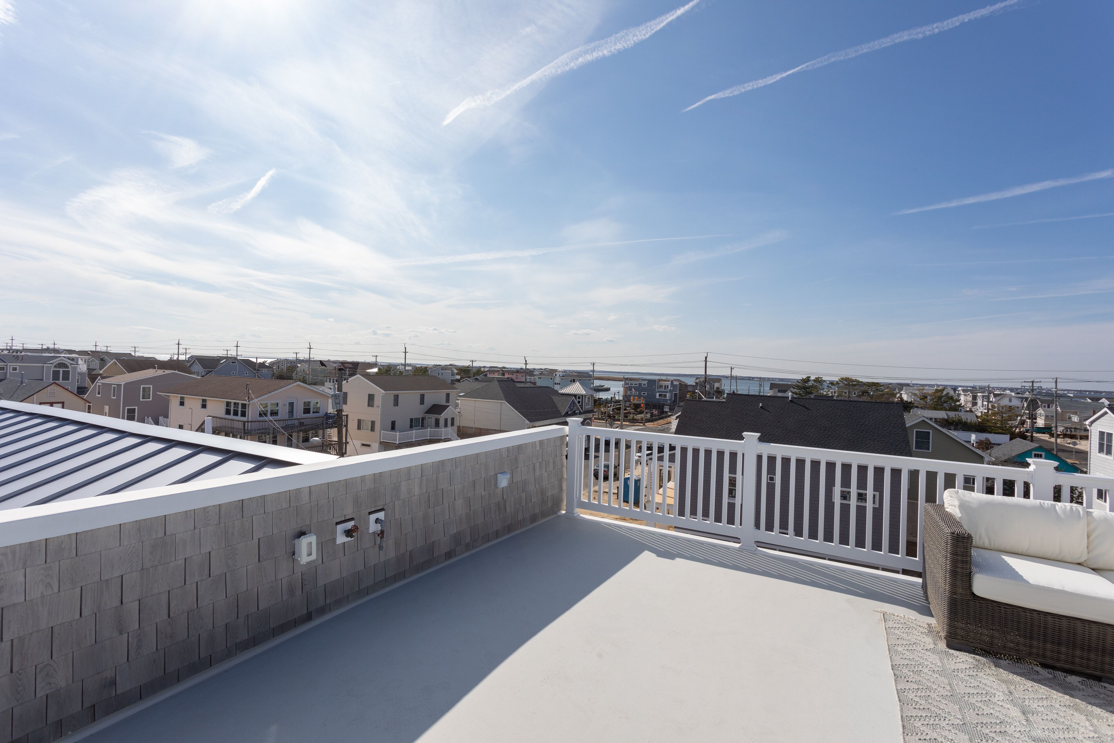 Terraza en la azotea con barandal blanco, sofá de mimbre y vistas a edificios residenciales.