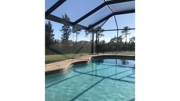 Une piscine aux eaux cristallines, protégée par un filet de sécurité, entourée d’une pelouse et d’arbres.