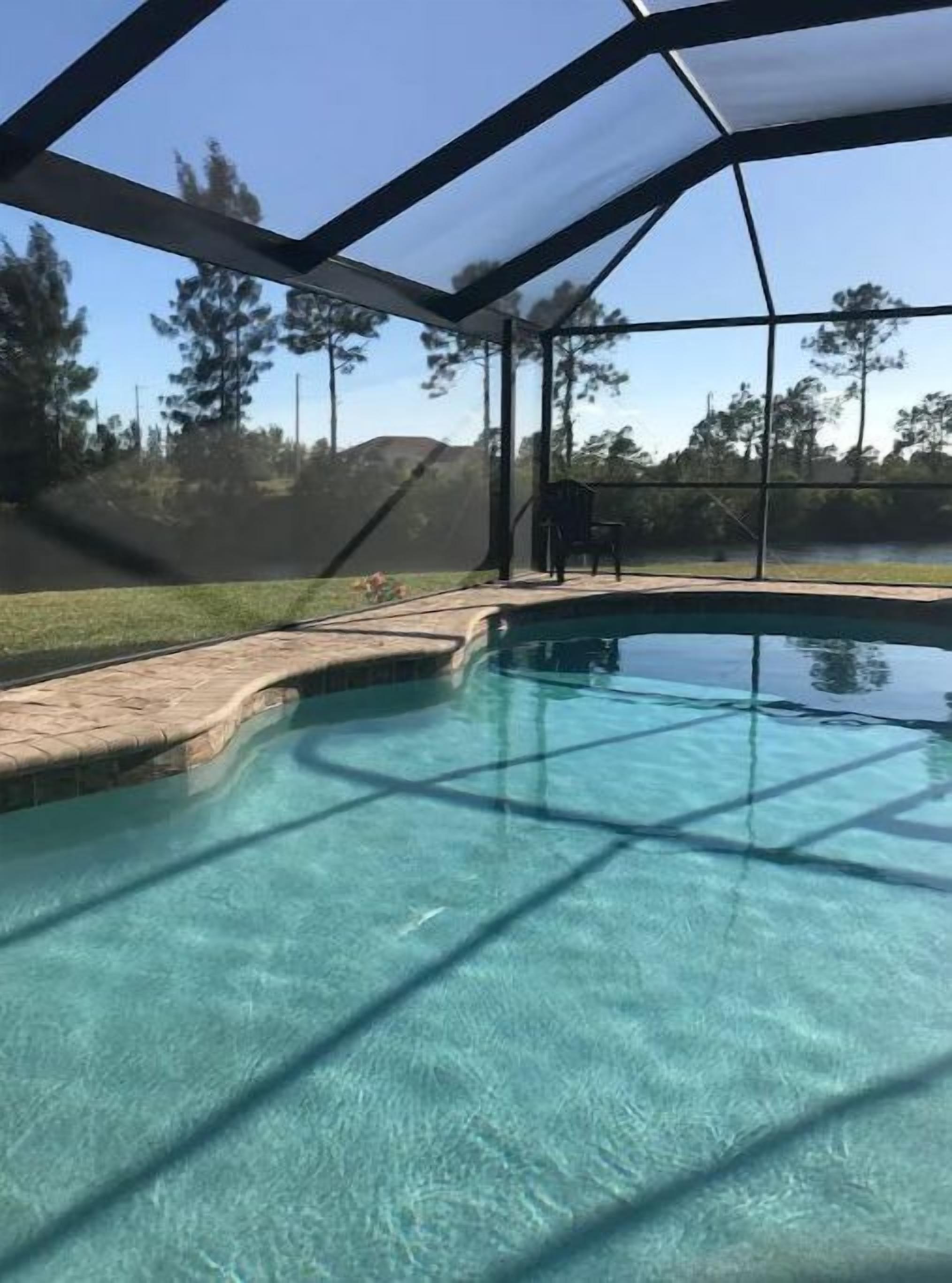 A clear swimming pool with a safety net enclosure, surrounded by a grassy area and trees.