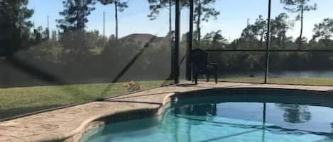 A clear swimming pool with a safety net enclosure, surrounded by a grassy area and trees.