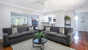 Ein modernes Wohnzimmer mit einem grauen Ecksofa, einem runden Couchtisch und einem Deckenventilator.