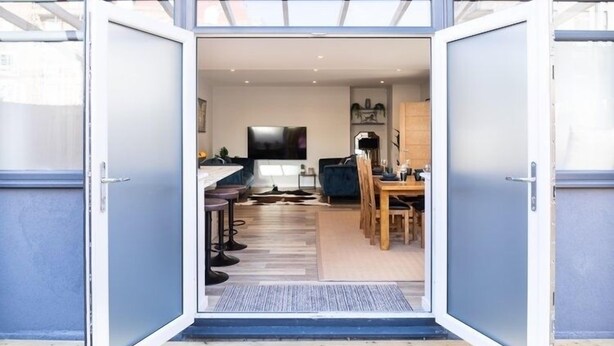 Porta aperta che dà su una cucina moderna con zona pranzo, televisore e divano.