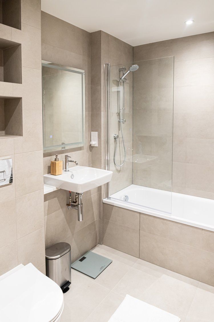 Een moderne badkamer met een douche met glazen wand, een witte wastafel en een ruime badkuip.