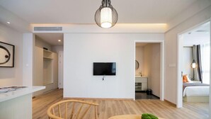 A modern hotel room with a wooden floor, a round table with a remote control, a television mounted on the wall, and a bed with a view of the outdoors. - Zhongjian Suisseplace Apart S Hotel (Shanghai)