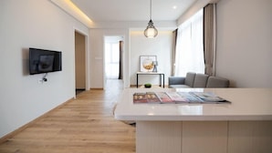 A modern living room with a flat-screen TV, a white coffee table with magazines, a hanging light fixture, and a sofa. - Zhongjian Suisseplace Apart S Hotel (Shanghai)