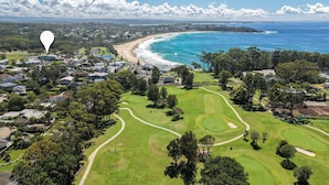 En vy från ovan av en golfbana vid kusten, med en strand och havet i bakgrunden.