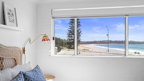 Ett rum med ett stort fönster med utsikt över en strand, en flätad fåtölj och en lampa.