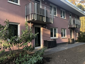 Um edifício com várias andares, varandas, entrada pavimentada e um pequeno jardim.