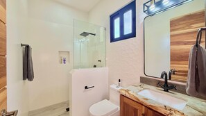A modern bathroom with a glass shower enclosure, a white toilet, a marble sink, and a wooden vanity.