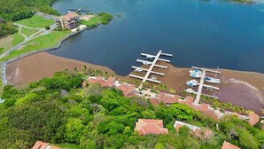 Vue aérienne d’une zone côtière avec un port de plaisance, des bateaux amarrés et une végétation luxuriante environnante.