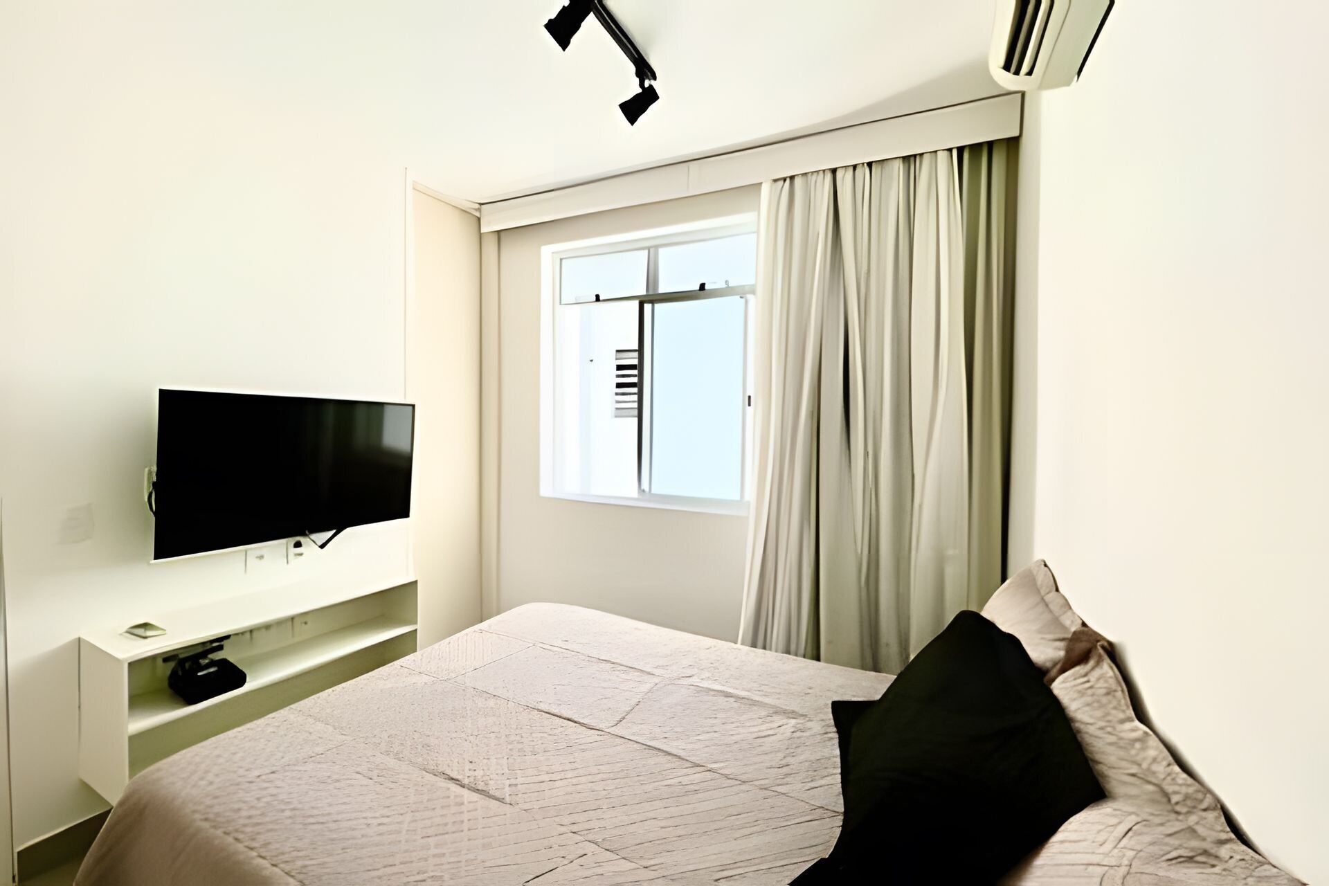 Habitación de hotel con cama, televisión de pantalla plana en la pared, ventana con cortinas y aire acondicionado.