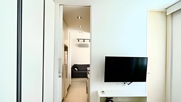 Een hotelkamer met een bed, een tv op een standaard, een deur en een gang die naar een badkamer leidt.