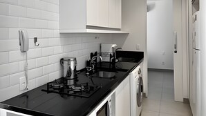 Een moderne keuken met witte kasten, een zwart aanrecht, een koffieapparaat, een spoelbak en een koelkast.