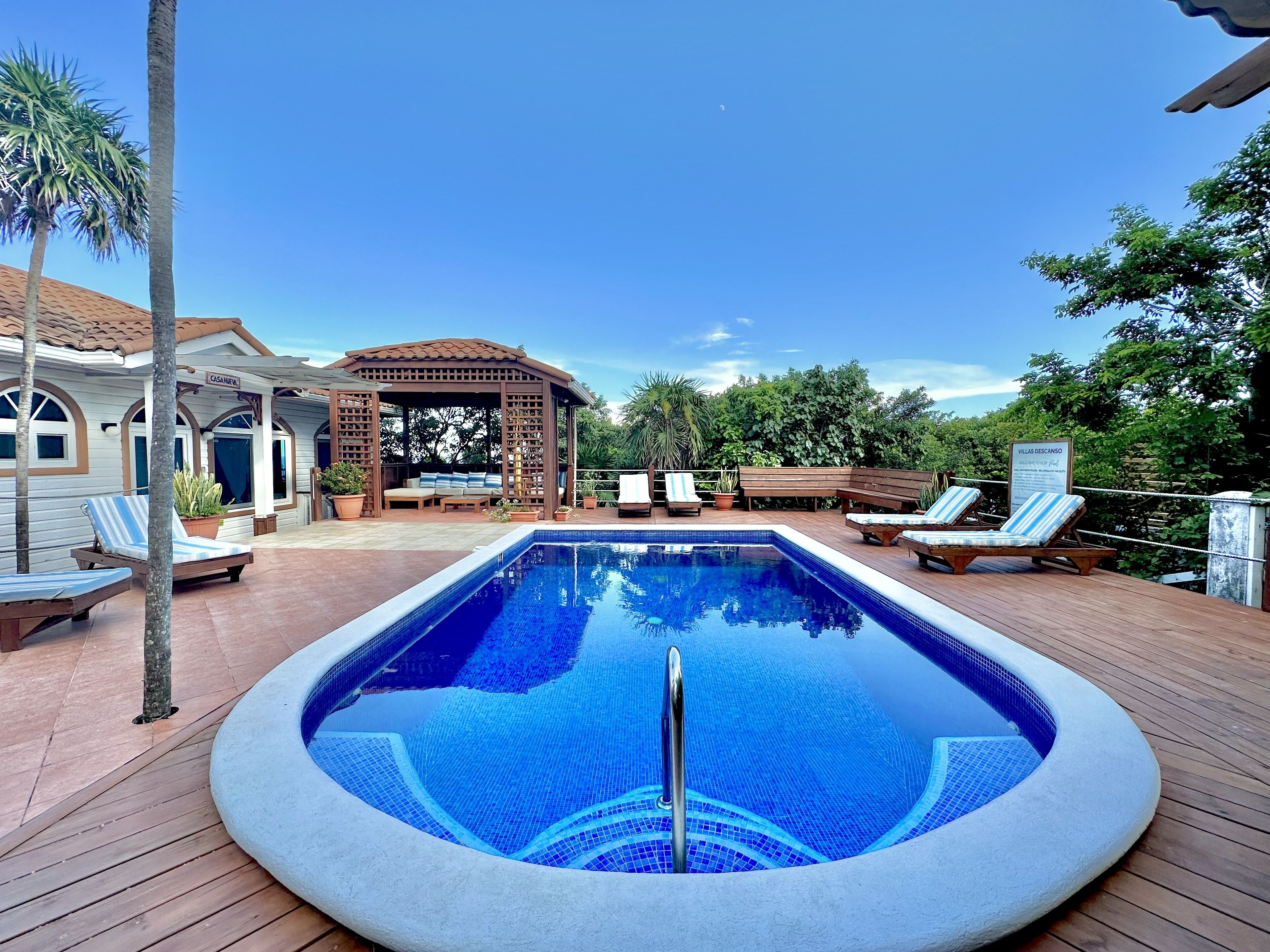 Una piscina con sillas de descanso y un área de estar cubierta.