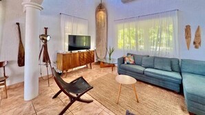 Un ampio soggiorno con una televisione grande, un divano blu e una ventola a soffitto.