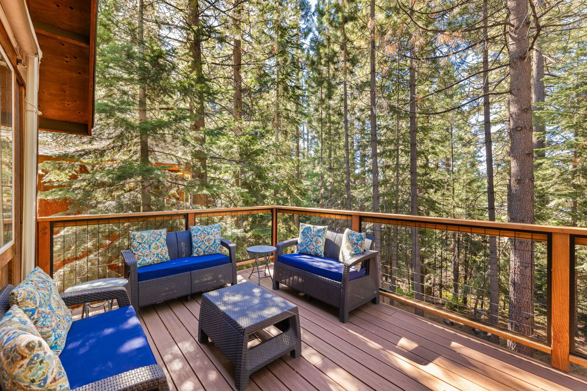 A deck with wicker furniture and blue cushions, surrounded by tall trees.