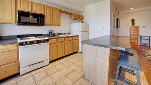 Una cocina con armarios de madera, microondas, estufa, refrigerador y un taburete de bar.