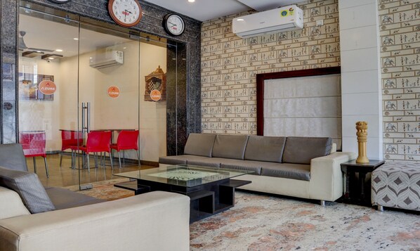 A modern lobby with a sofa, red chairs, a glass coffee table, and a patterned wall. - Treebo Azure (Varanasi)