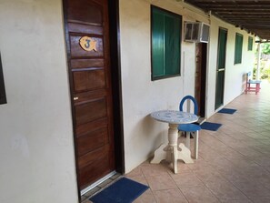 Un pasillo con una puerta de madera numerada con el 3, una pequeña mesa y una silla azul, y un suelo de baldosas.