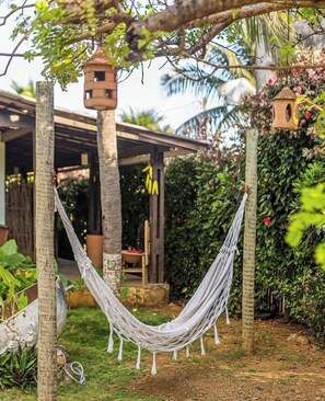 Una hamaca colgando entre árboles en un jardín con una estructura de madera y casas para pájaros al fondo.